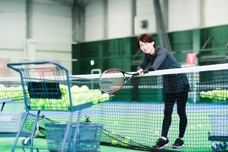 テニスコートでネットに腕を乗せている女性