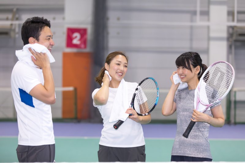 テニスコートで汗を拭く女性2名と男性1名